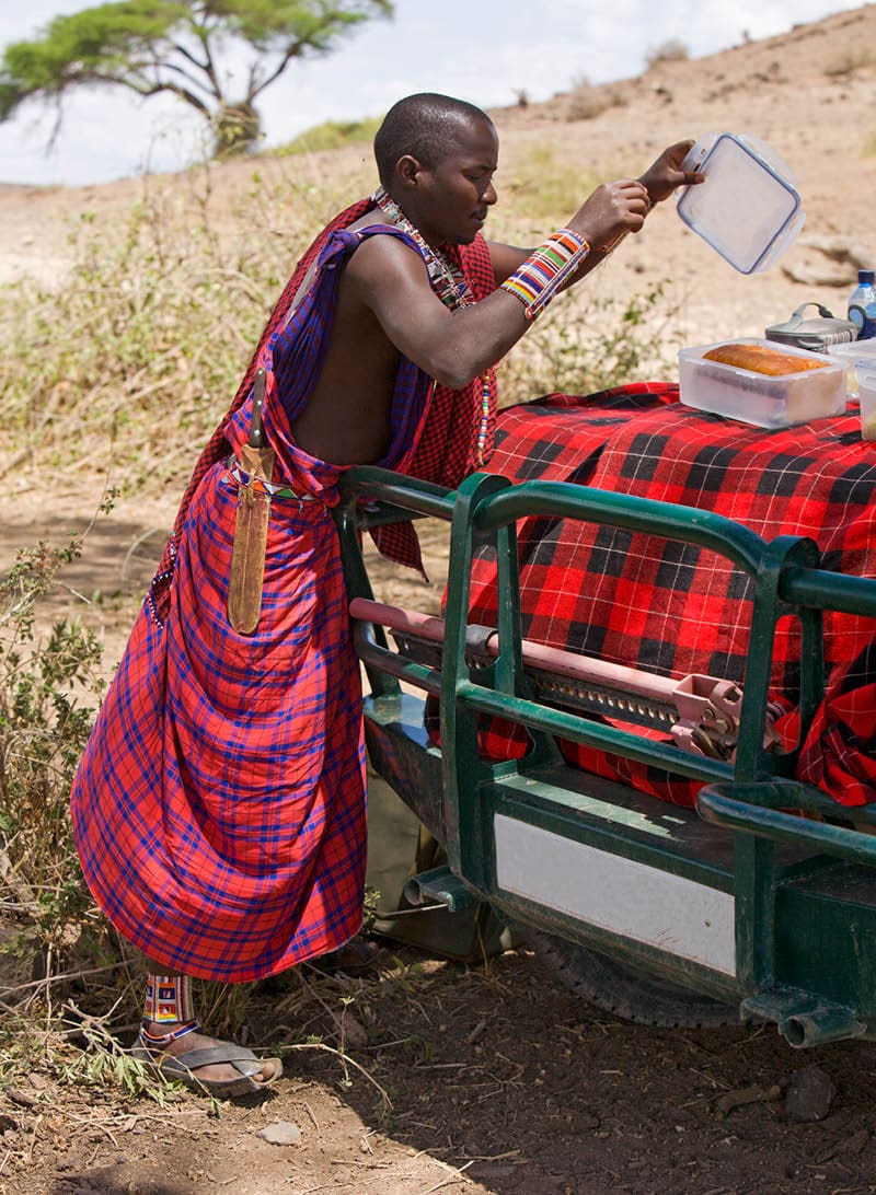 Young masai warrior preparing a picknic on the hood of the car.See also my LB: