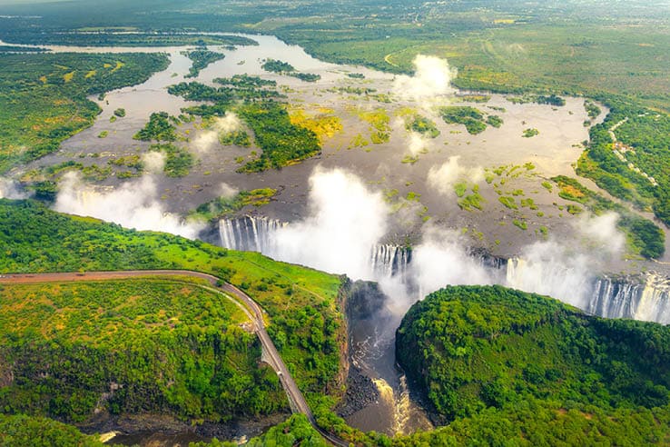 Victoria Falls in Zimbabwe and Zambia, Aerial helicopter photo, green forest around amazing majestic waterfalls of Africa. Livingston Bridge above the river