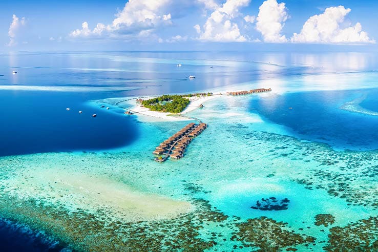 Panoramic aerial view of a turquoise coral reef and lagoon with a tropical paradise island and calm sea at the Maldives, Indian Ocean