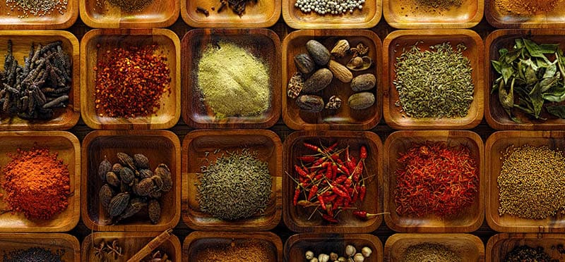 A large selection of commonly used Indian cooking spices in wooden trays on an old table. Spices include, chili ,cumin, tumeric, corriander, cumin, cardamon, garam masala, saffron, cinamon and star anise, poppy seed, sesame, cloves, nutmeg, black and white pepper corns, aniseed and fenugreek.