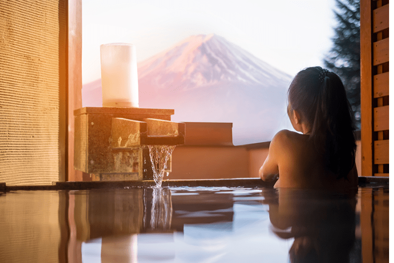 Beautiful woman enjoy onsen (mineral hot bath) in morning and seeing view of Fuji mountain in japan 