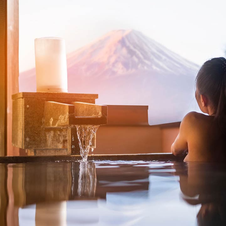 Beautiful woman enjoy onsen (mineral hot bath) in morning and seeing view of Fuji mountain in japan 