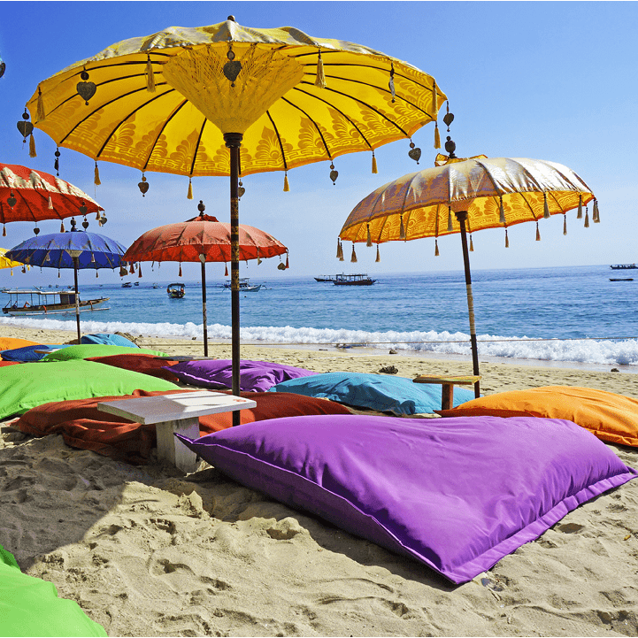 This image shows some colourful beach umbrellas and sand pillows in a pristine tropical beach bathed by the Bali sea.