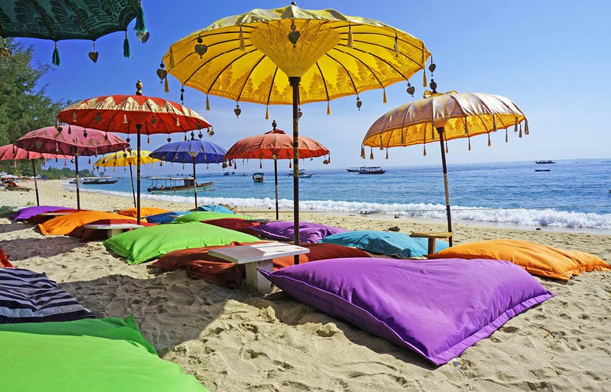 This image shows some colourful beach umbrellas and sand pillows in a pristine tropical beach bathed by the Bali sea.