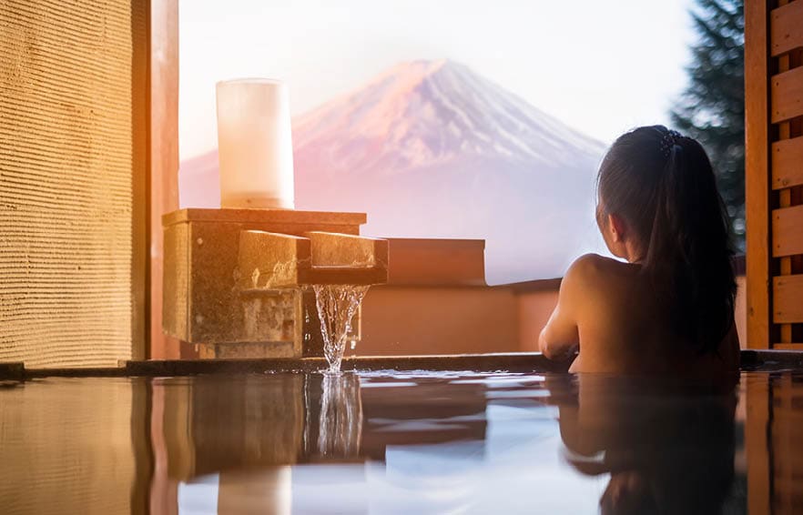 Beautiful woman enjoy onsen (mineral hot bath) in morning and seeing view of Fuji mountain in japan 