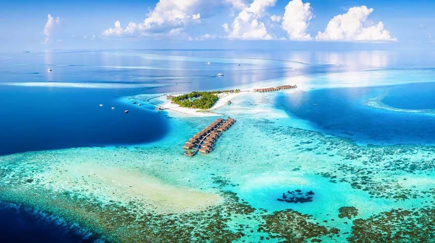 Panoramic aerial view of a turquoise coral reef and lagoon with a tropical paradise island and calm sea at the Maldives, Indian Ocean