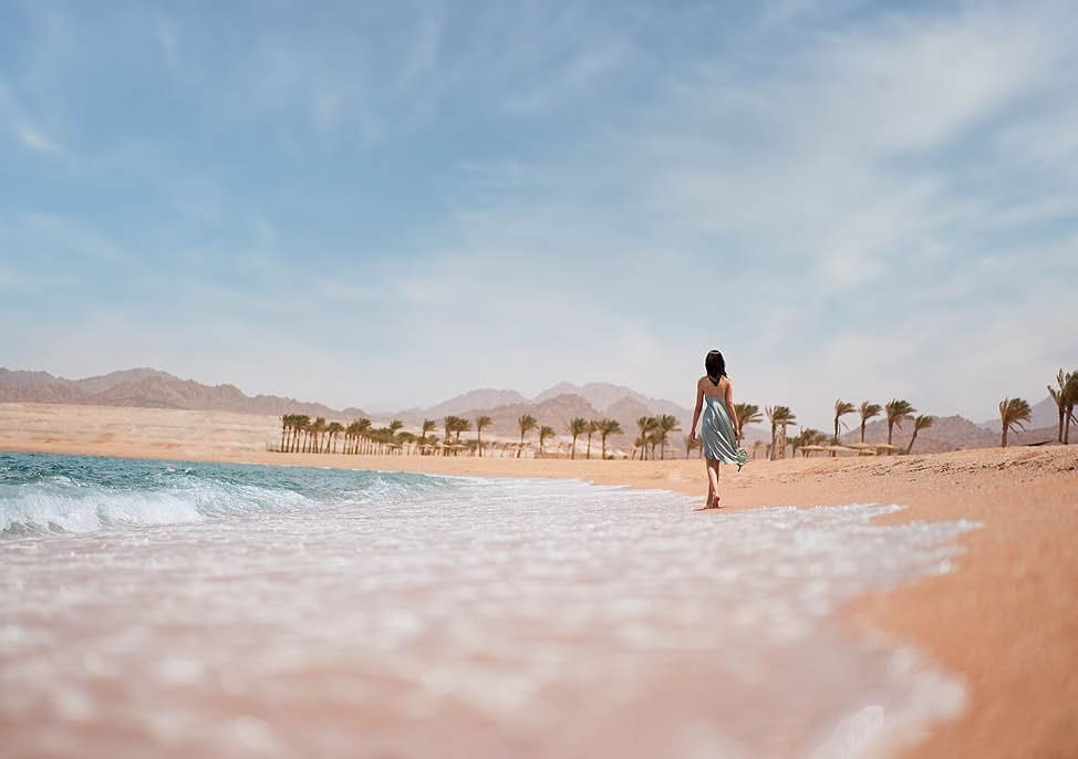 Attractive young woman walks barefoot along the seashore at sunset