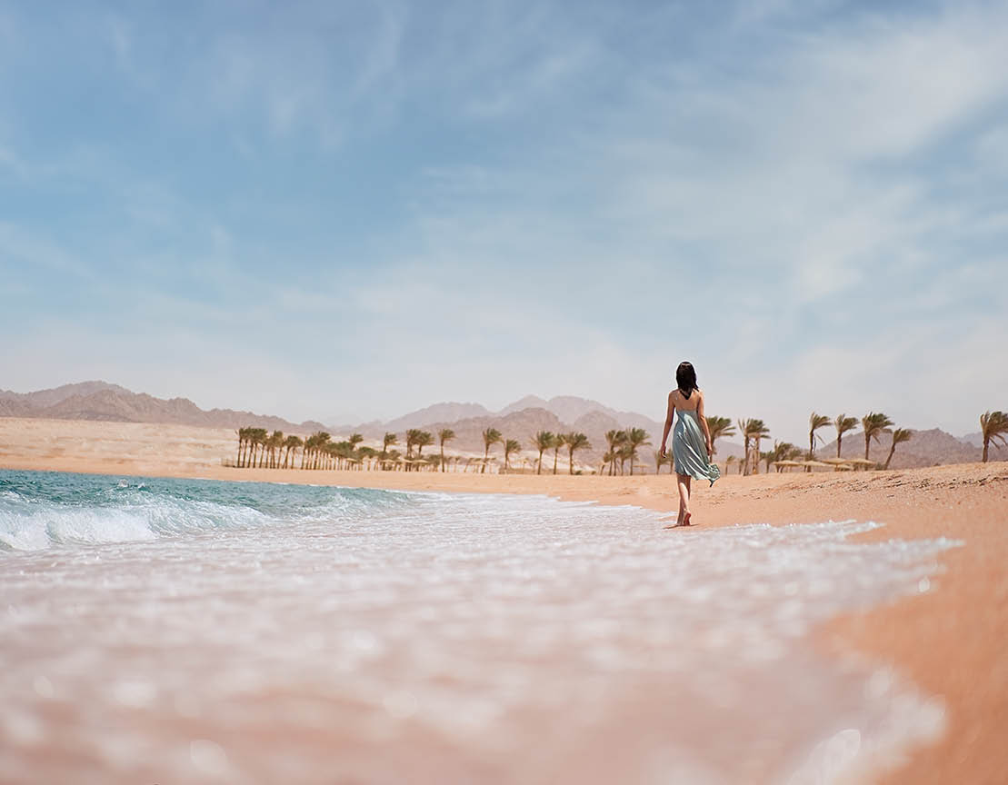 Attractive young woman walks barefoot along the seashore at sunset