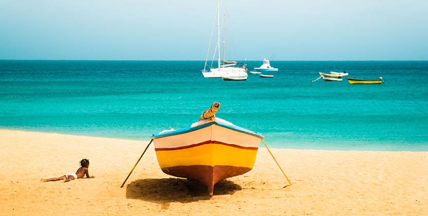 Cabo Verde No Stress. Sunny tropical Sal island vacation background of African child silhouette enjoying sandy Santa Maria beach with colourful boats and turquoise water seascape on Cape verde islands