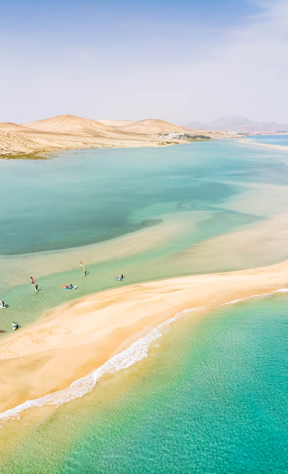 Aerial view of beach in Fuerteventura island with windsurfers learning windsurfing in blue turquoise water during summer vacation holidays, Canary islands from drone