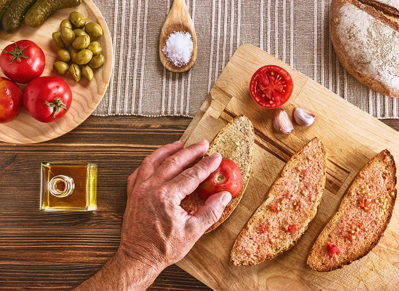 Action of rub the tomato on the bread with the hand.