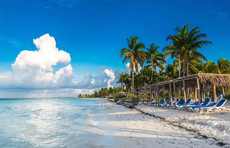A seat in front of the Caribbean sea. Beautiful beach of Cayo Gulliermo, in Cuba, next to the coral reef, with palm trees and long chairs where to chill out enjoying the breeze and the sun.