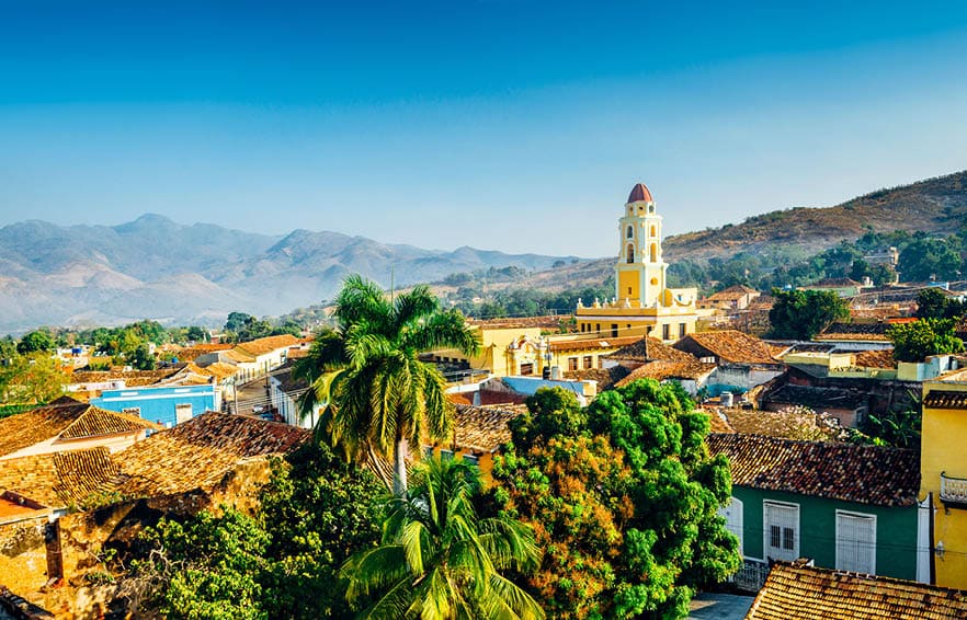 Panoramic view over the city of Trinidad, Cuba with mountains in the background and a blue sky. The bell tower belongs to the Iglesia y Convento de San Francisco.