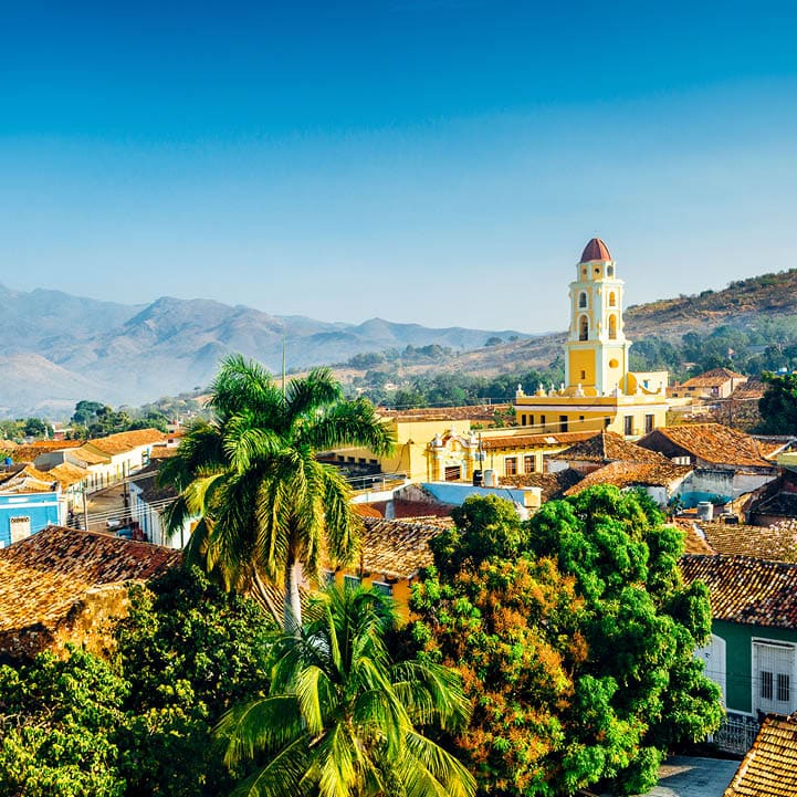 Panoramic view over the city of Trinidad, Cuba with mountains in the background and a blue sky. The bell tower belongs to the Iglesia y Convento de San Francisco.