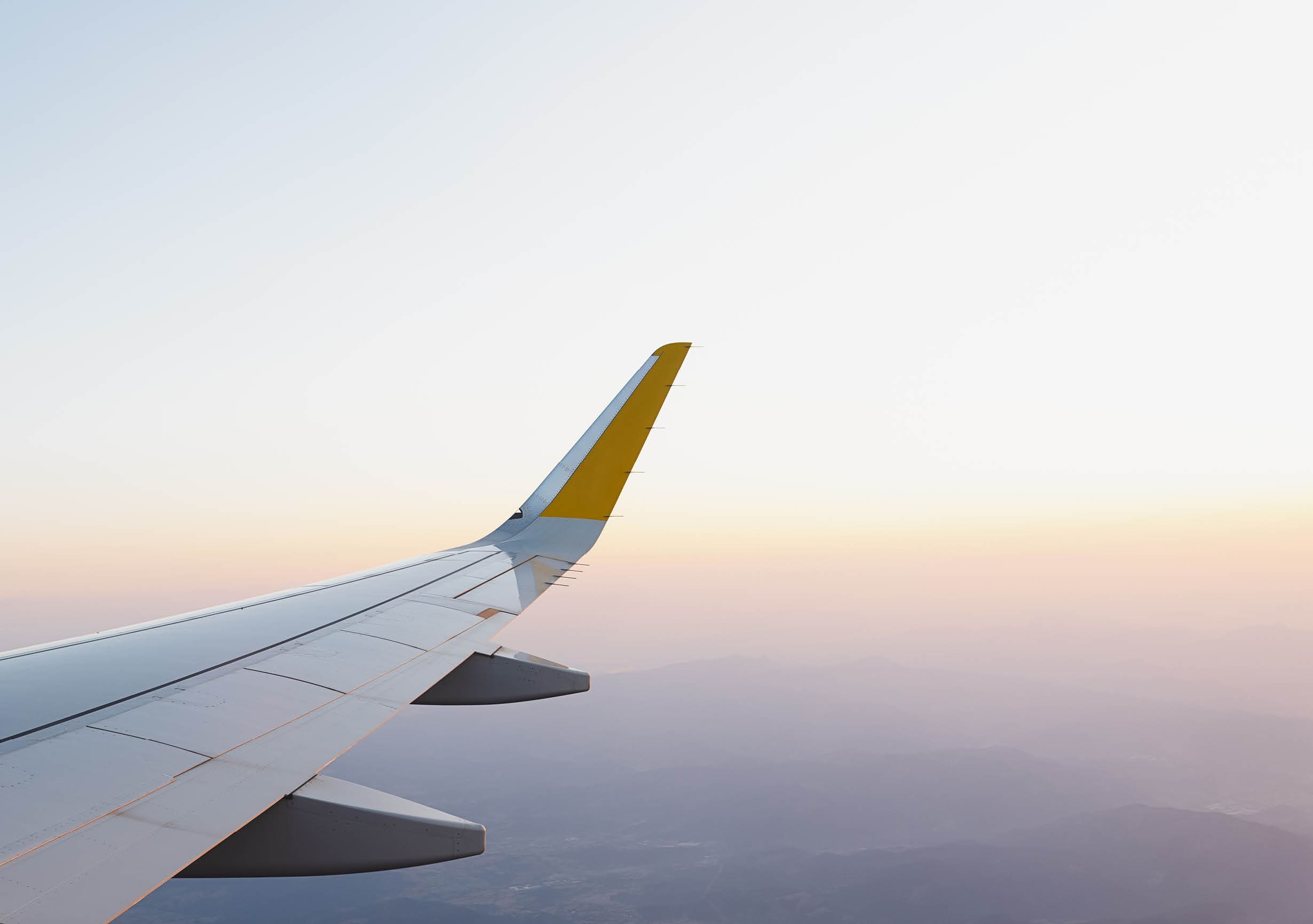 Wing of modern aircraft flying in cloudy blue sky during trip