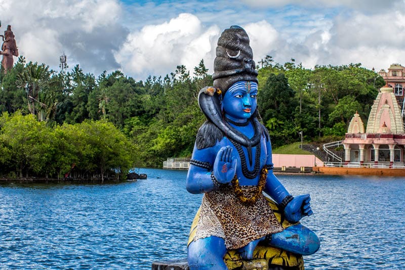Blue Shiva statue on the background of the Indian temple and tropical greenery