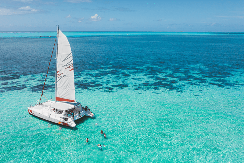 Family and friends swimming near a beautiful catamaran in the paradise turquoise lagoon of the east coast of Mauritius