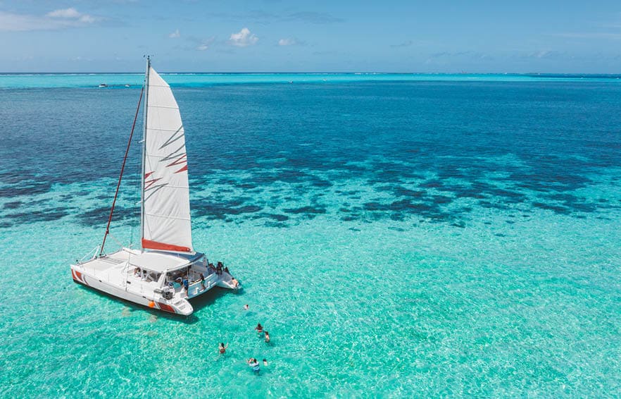 Family and friends swimming near a beautiful catamaran in the paradise turquoise lagoon of the east coast of Mauritius