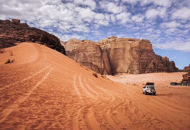 red sand dune surrounded by wind-beaten mountains, beautiful cloudy sky, Wadi Rum desert, Jordan                           