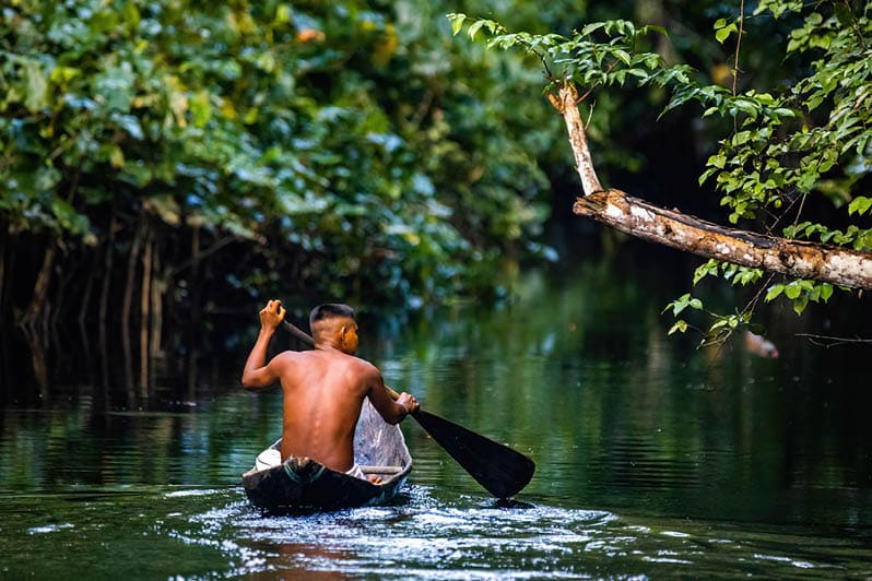 Native tribal man swimming in amazonia rainforest in handmade boat