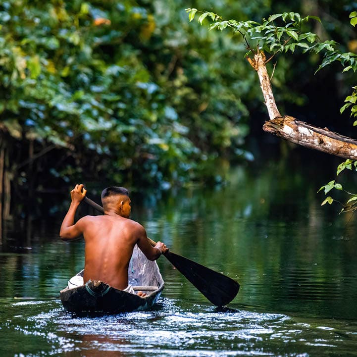 Native tribal man swimming in amazonia rainforest in handmade boat