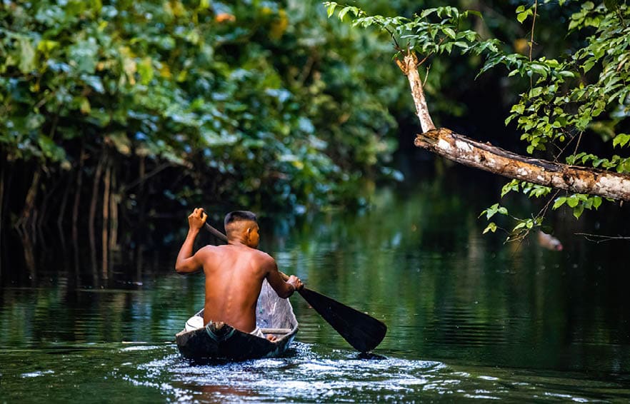 Native tribal man swimming in amazonia rainforest in handmade boat