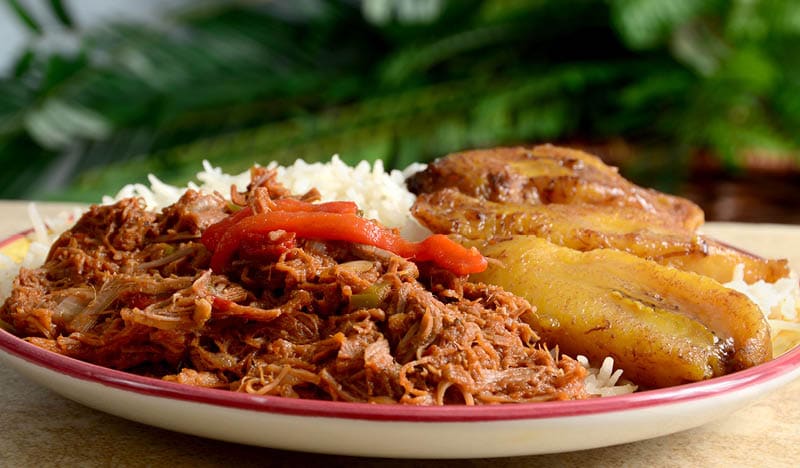 Ropa Vieja is a classic Cuban stew of shredded beef, served here with white rice and fried plantains.