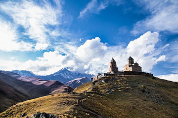 Gergeti Tsminda Sameba church in Kazbegi (Stepantsminda) village, Georgia, Europe. Fall sunset, white clouds above the church.