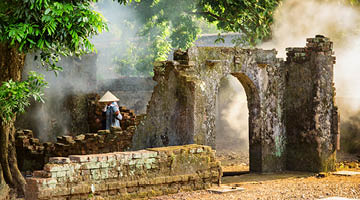 Unknown Vietnamese woman in traditional bamboo hat among scenic ruins of old buildings at the Tu Duc Royal Tomb in Hue, Vietnam. Hue is a popular tourist destination of Asia.