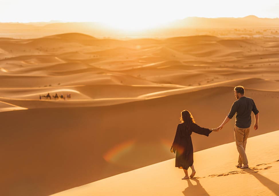 Couple walking in Sahara desert at sunset. View from behind, nature background. Travel, freedom and wanderlust concept.