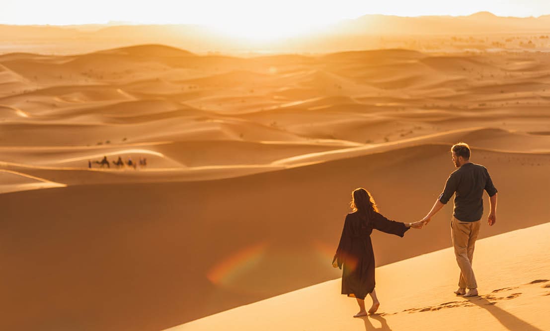 Couple walking in Sahara desert at sunset. View from behind, nature background. Travel, freedom and wanderlust concept.