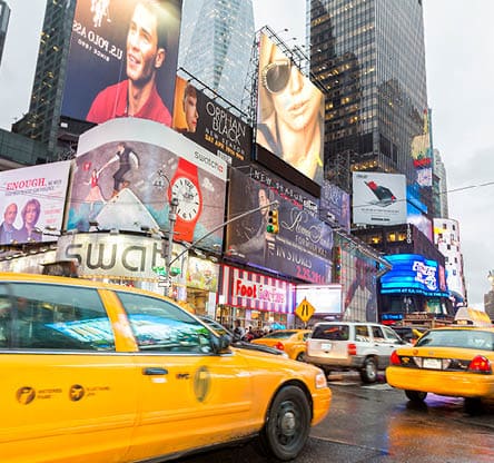 Yellow taxi cabs in traffic on 7th Avenue at Times Square, Broadway, Midtown Manhattan, New York City. Times Square is is brightly lit by neons and billboards and is part of the theater district in Manhattan. It is also one of the main tourist attractions of the city with nearly 40 million tourists visiting it yearly.