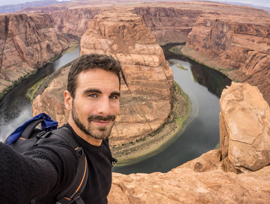 A young happy traveler taking a selfie. Horseshoe Bend on the Background. Page, Arizona